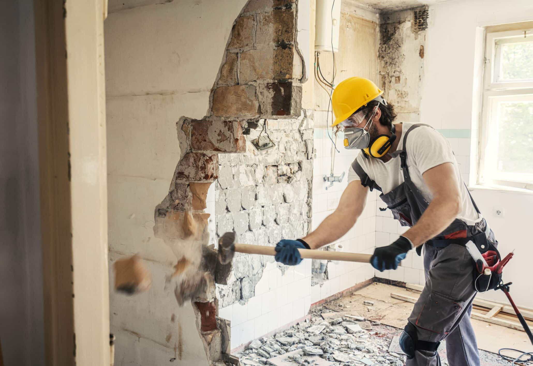 Bauhelfer in Arbeitsschutzkleidung beim Abreißen einer Mauer