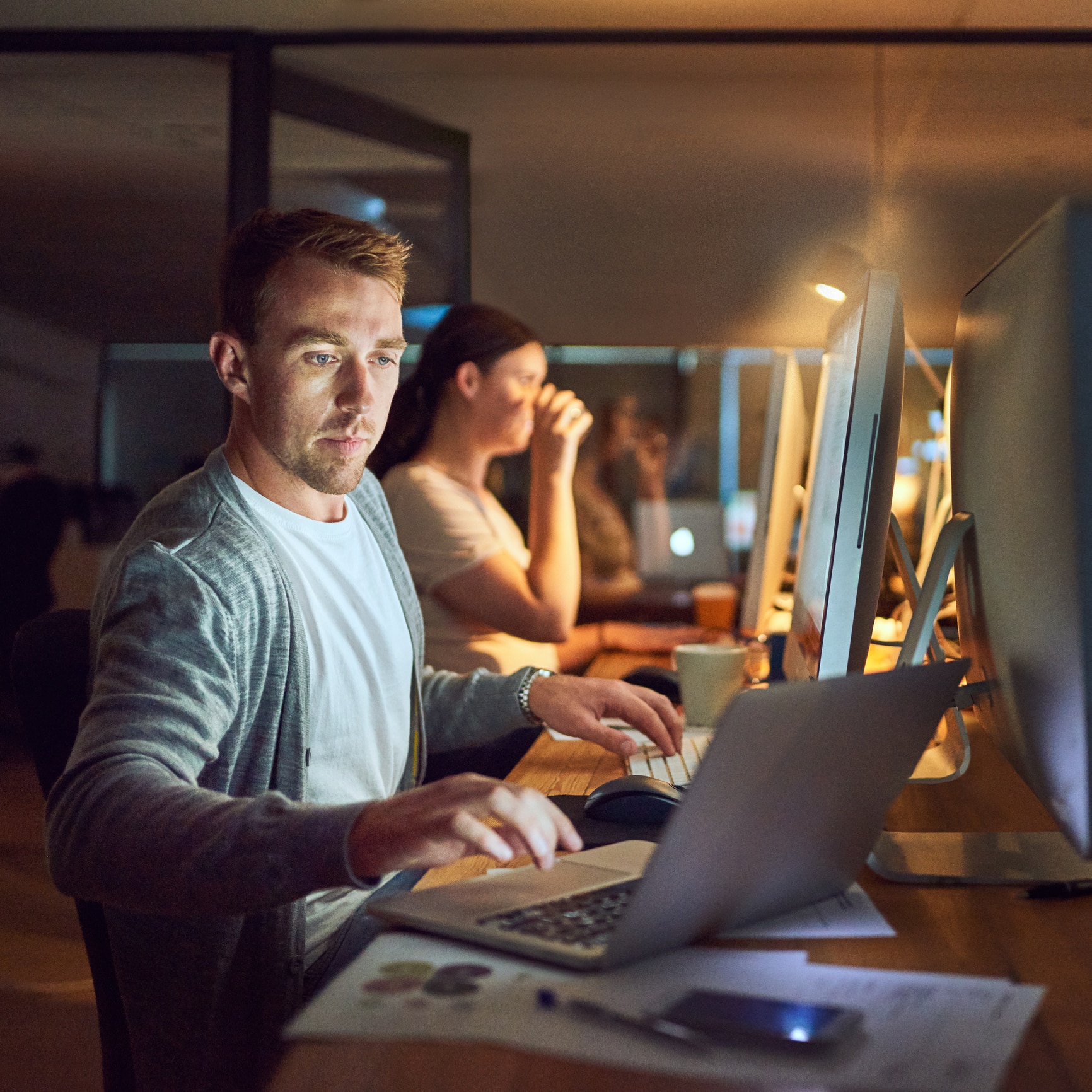 Portrait eines jungen Mannes bei der Arbeit vor dem PC und Laptop in Büroumgebung