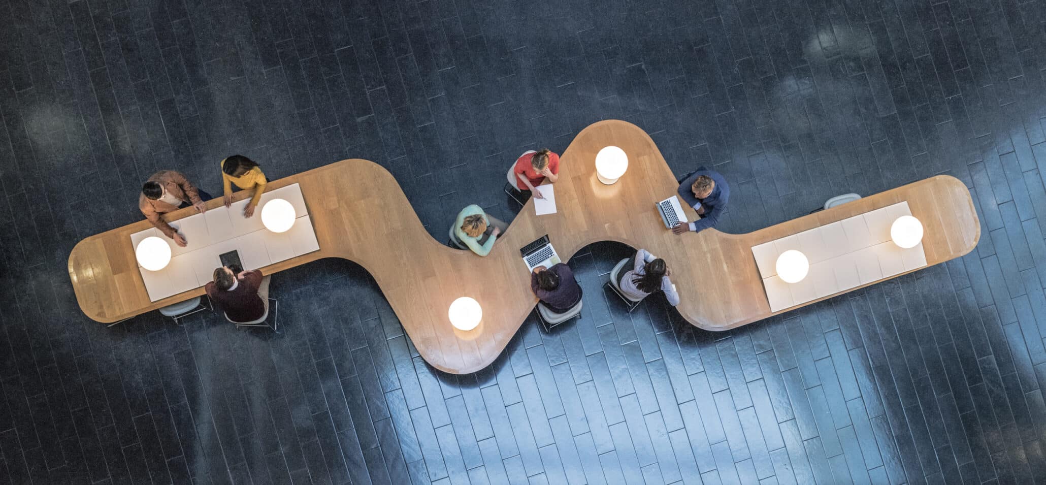Vogelperspektive auf einen langen Schreibtisch mit Büroarbeitern in einem Business Meeting Raum