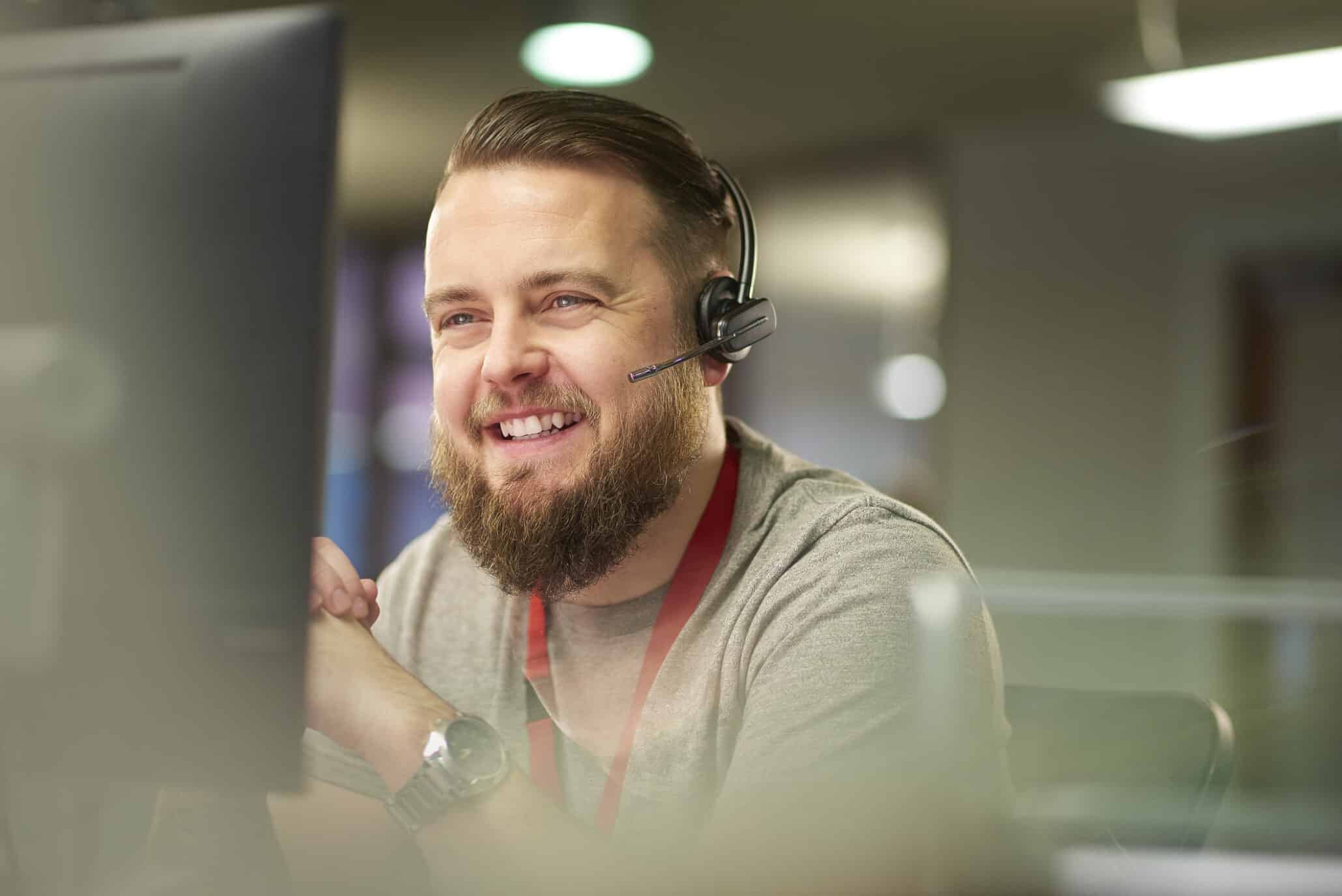 Lächelnder Mann mit Headset vor einem Monitor als Kundenberater und Call-Center Agent