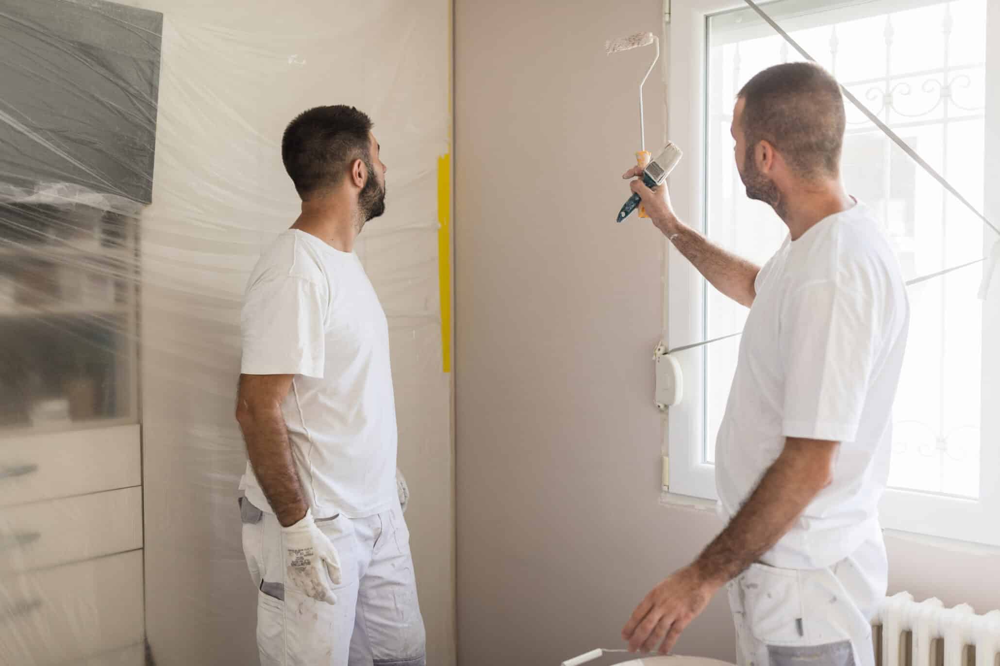 Zwei Maler in Arbeitskleidung bei der Renovierung einer Wand