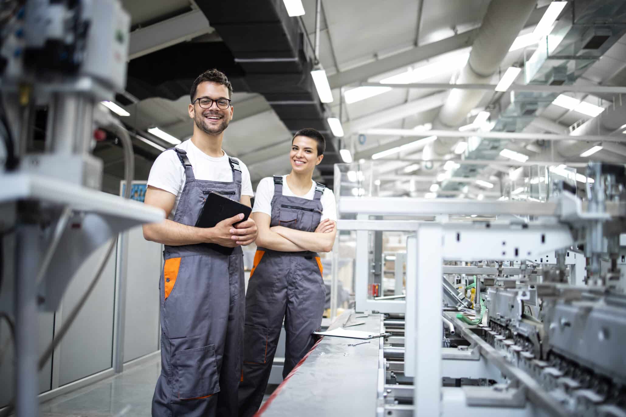 Zwei junge Menschen während ihres Zeitarbeiteinsatzes als Maschinenbediner an einer Maschine in einer Industriehalle