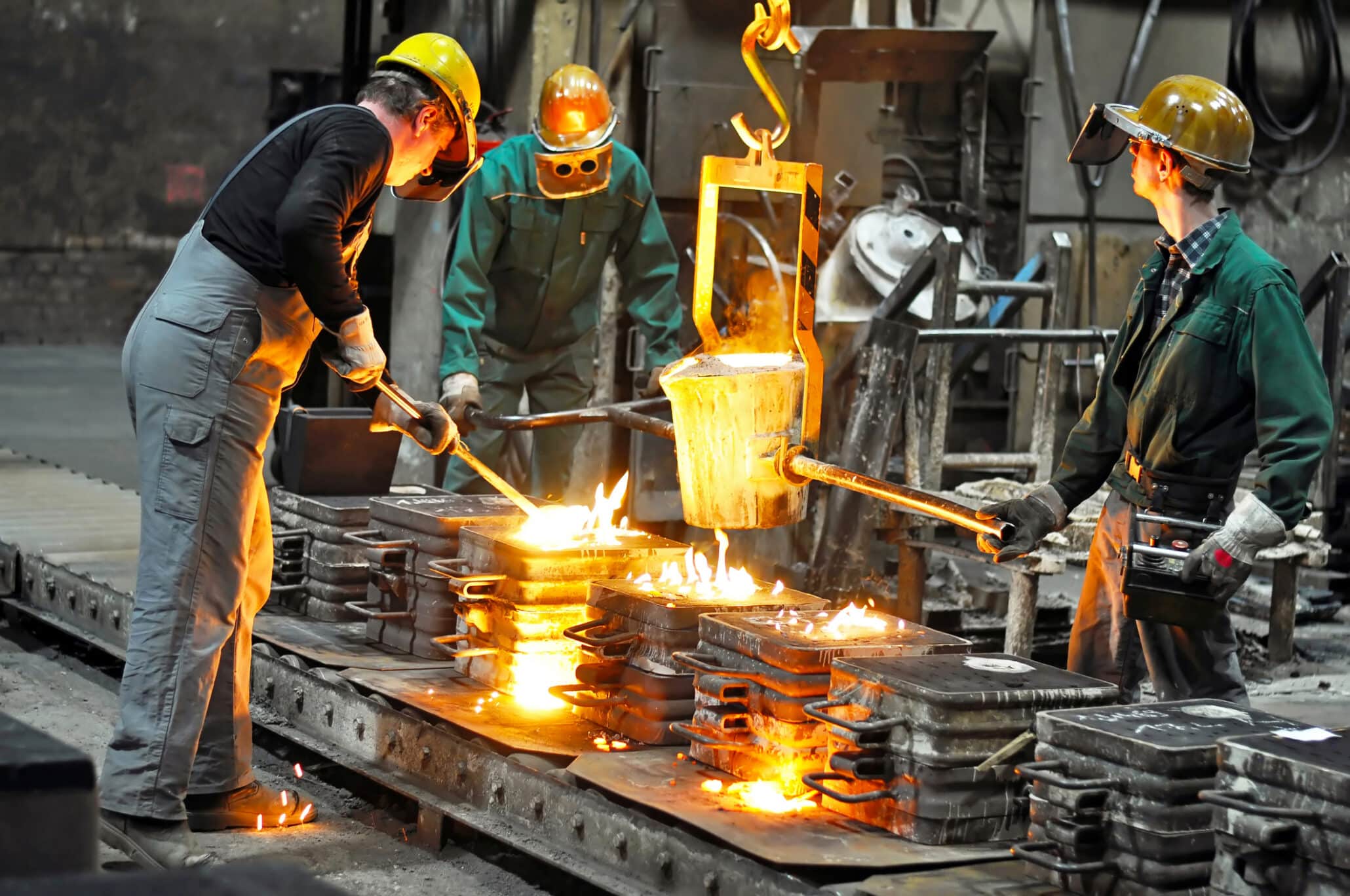Drei Zeitarbeiter in Arbeitsschutzkleidung in einer Gießerei beim Metallgießen