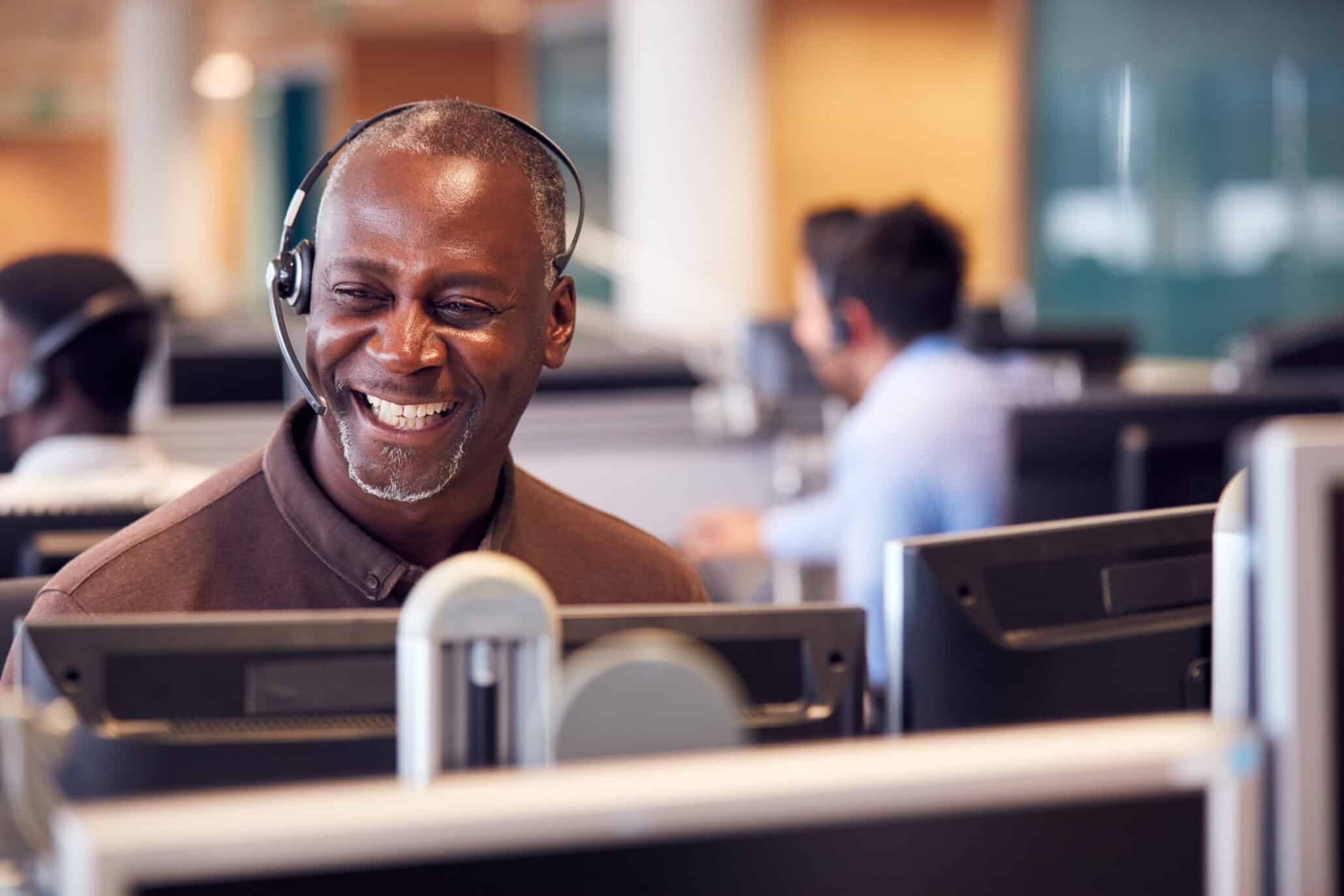 Portrait eines Mannes mit Headset vor seinem Monitor in einem Call Center