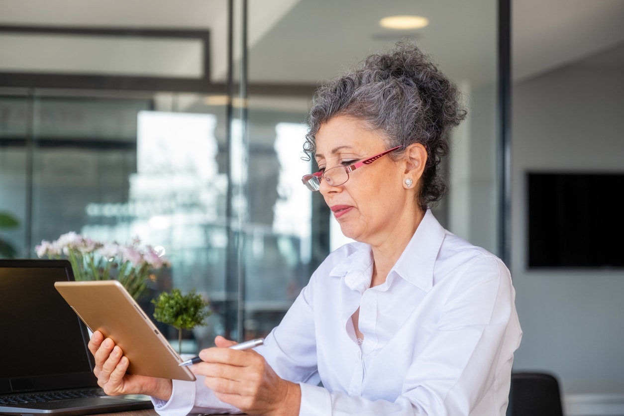 Ältere Frau mit Brille schaut auf ihr Tablet während ihres Zeitarbeiteinsatzes als Bürokauffrau