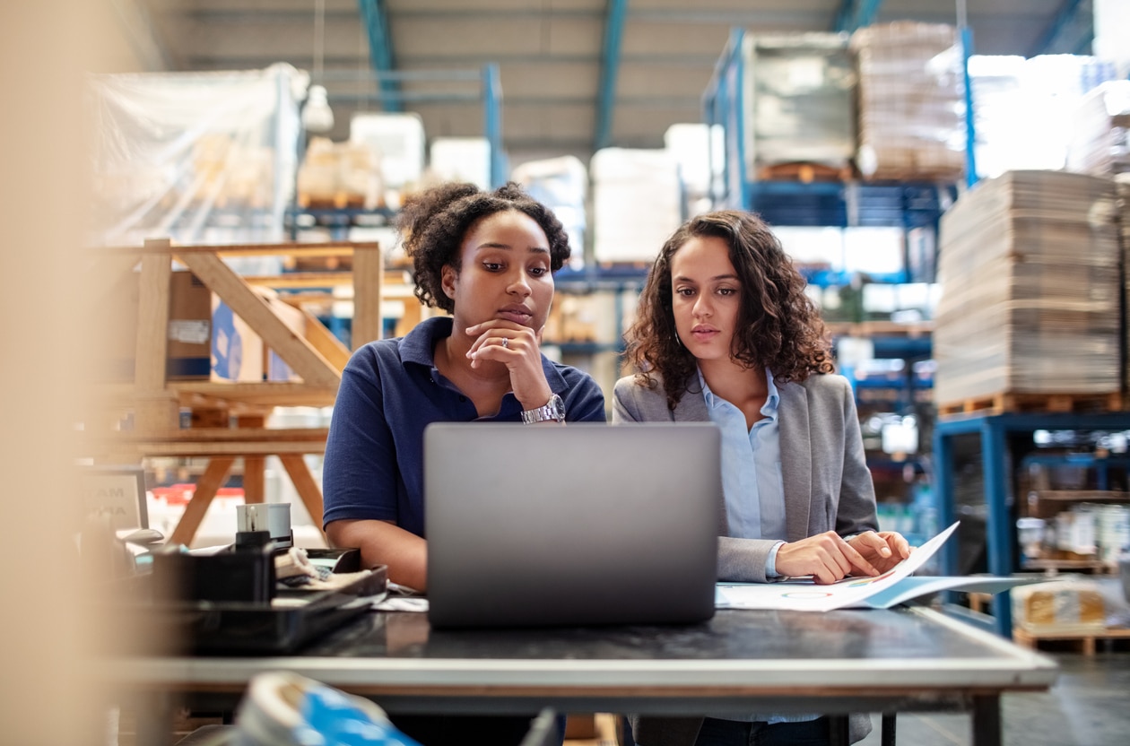 Zwei Frauen vor einem Laptop im Warenlager beim Prüfen der Wareneingänge