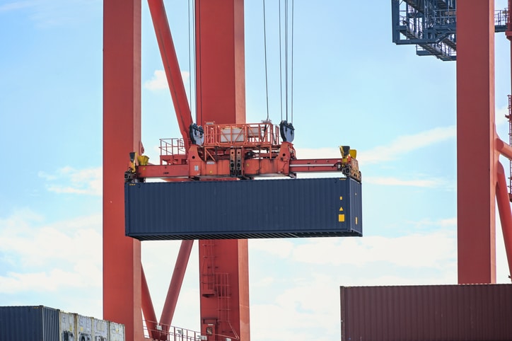 Blauer Container wird von einem roten Kran im Industriehafen von Hamburg nach oben gezogen