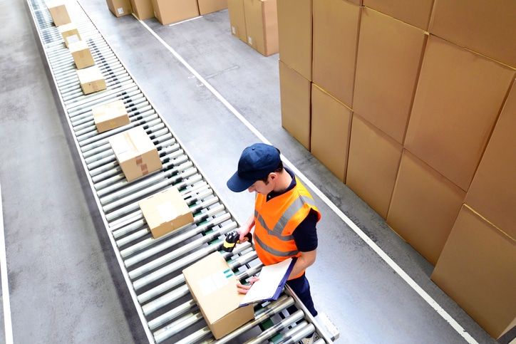 Draufsicht auf ein Rollband voller Pakete, die ein Mann während seines Zeitarbeit-Einsatzes in einem Paketlager scannt